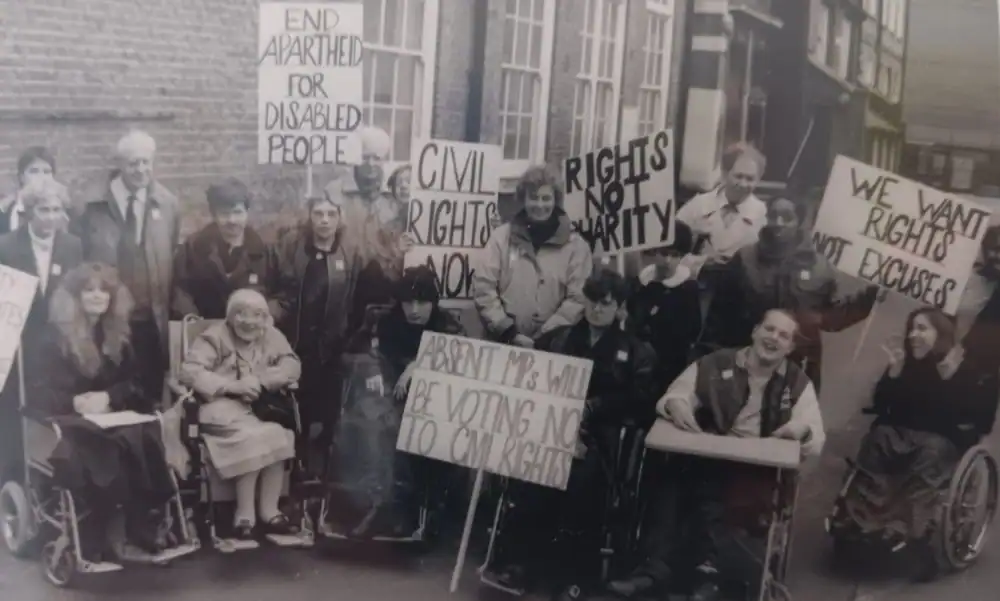 A group of disabled people hold signs demanding civil rights and an end to discrimination during a protest outside a building.