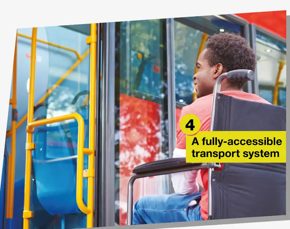 A man in a wheelchair waits to board a city bus via a ramp; a sign nearby reads “4 A fully-accessible transport system.”.