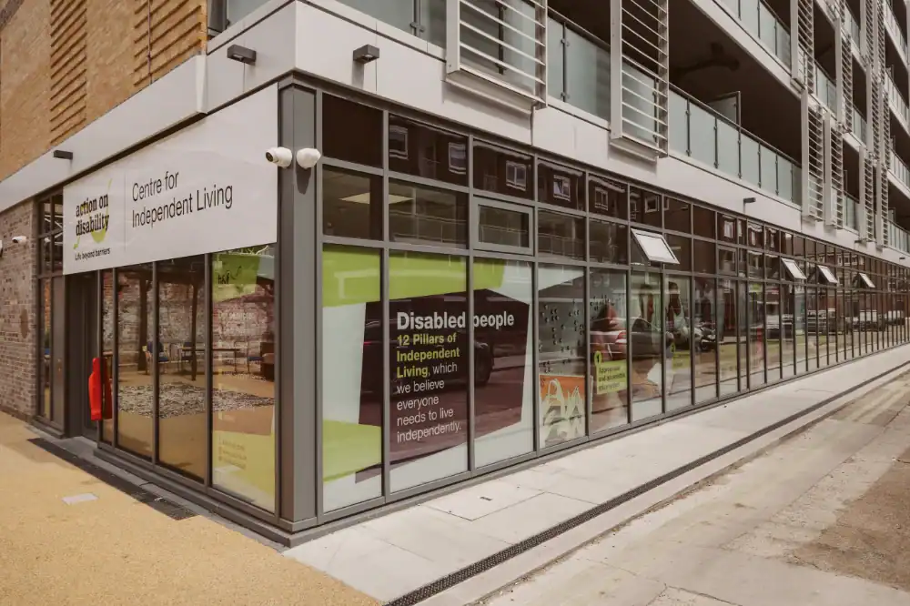 Modern building with glass walls housing the Centre for Independent Living; signs about support for disabled people are visible through the windows.