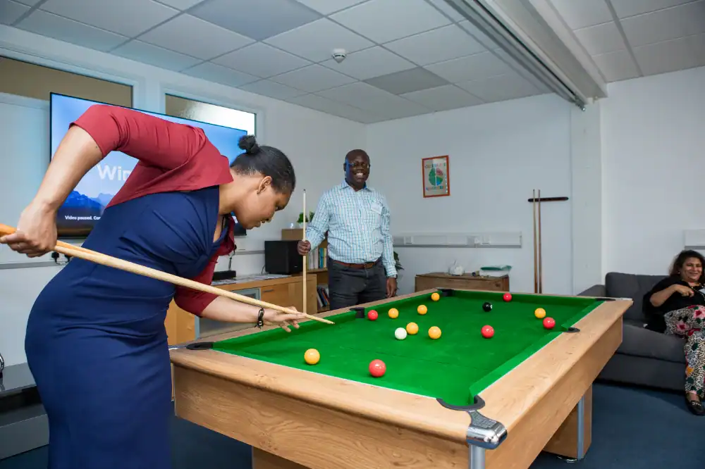 A woman bends to take a shot at a pool table while a man and another woman watch in a casual indoor setting.