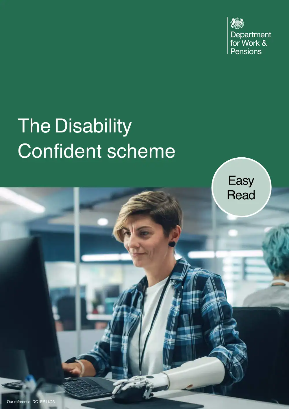 A person with a prosthetic hand works at a computer in an office. The cover text reads: "The Disability Confident scheme. Easy Read. Department for Work & Pensions.